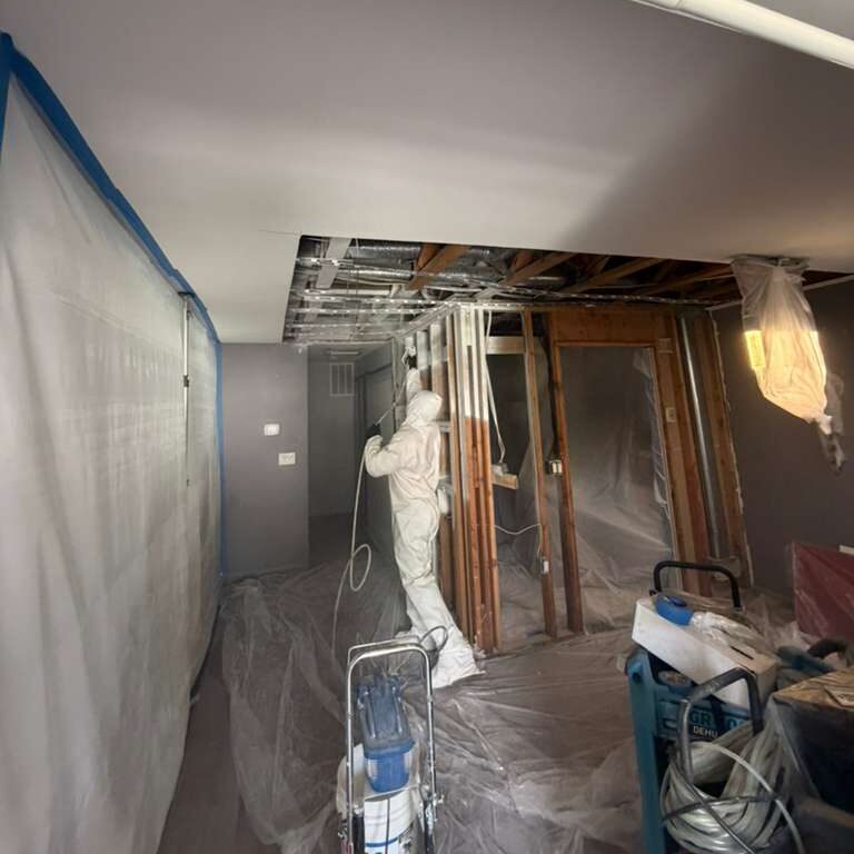 Worker in protective suit spraying ceiling during renovation